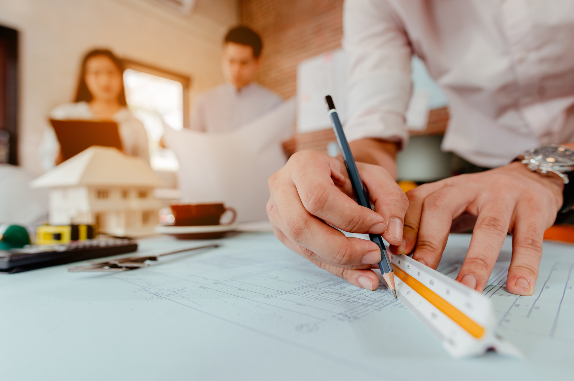 Close up of male architect hands writing model on the desk. Blurred behind team of engineer discussing of construction plan. Engineer, Engineering, Architecture, Design, Planning, Occupation concept.